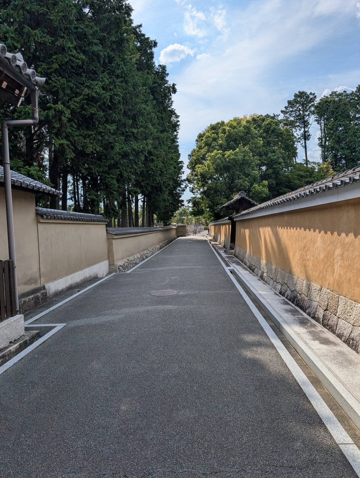 墓地へ続く道。土塀の向こうに現代の建物が見える