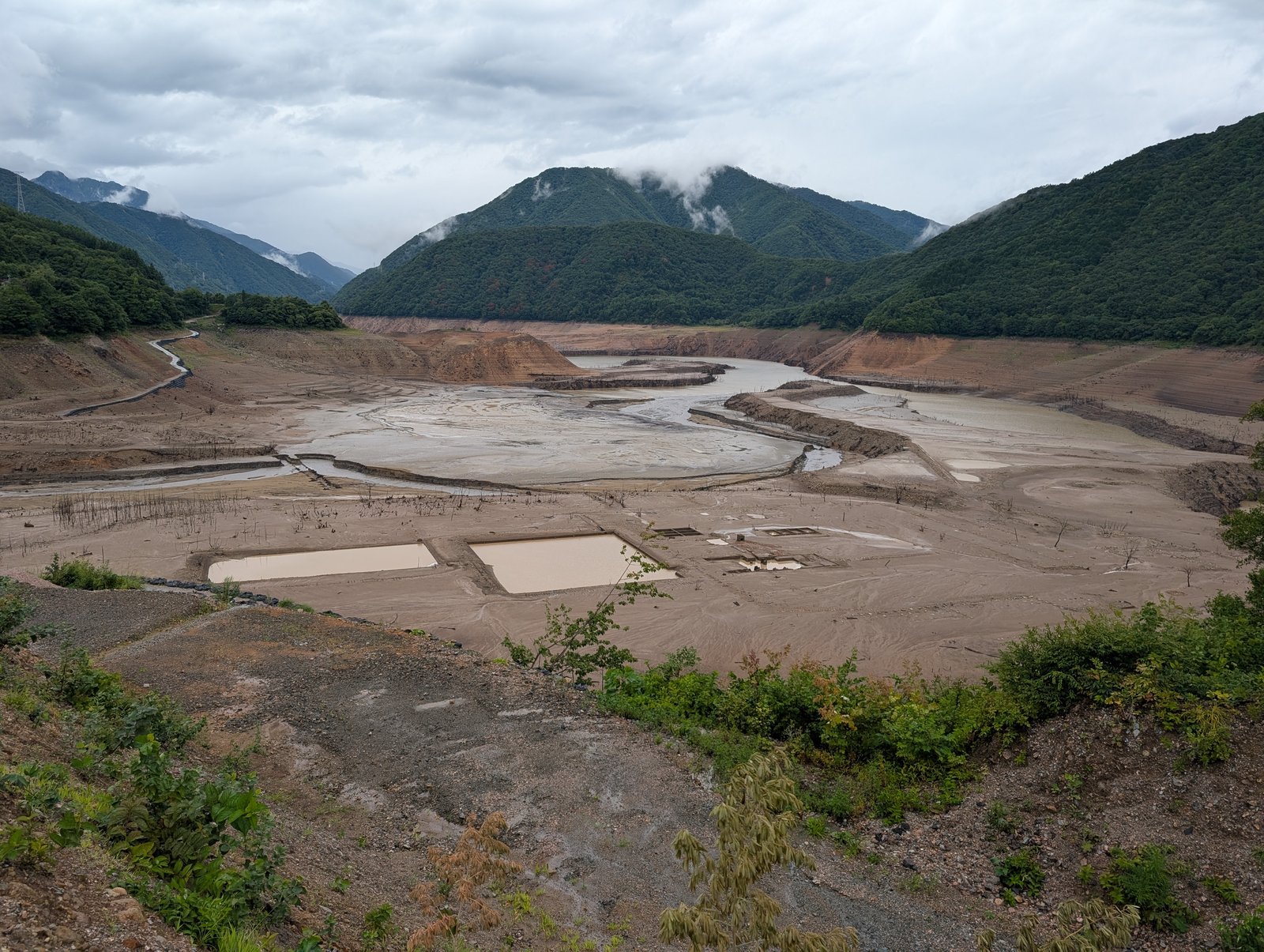 水の引いた御母衣湖。平らな砂泥地に四角い区画がいくつも見え、立ち枯れの木が点々と残る