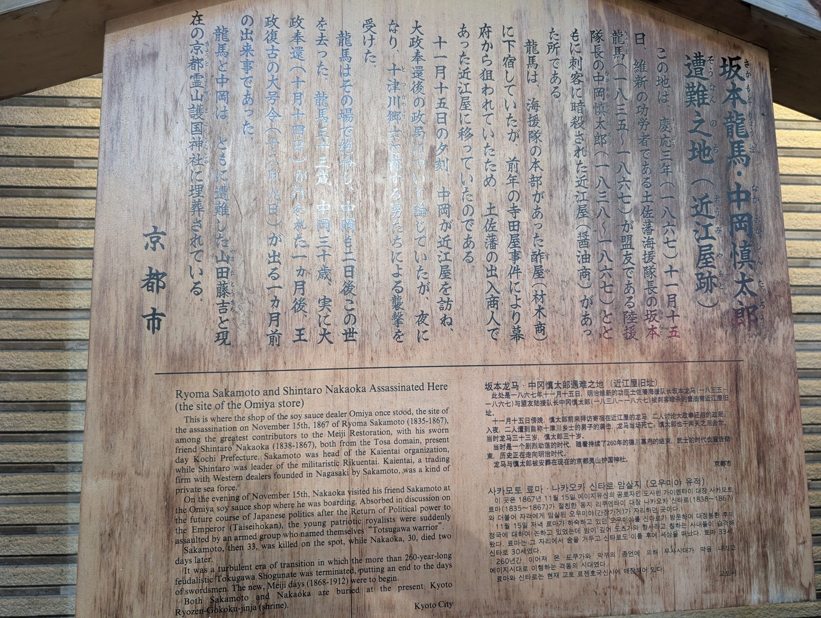 石標の後ろに掲げられた京都市の説明板「坂本龍馬・中岡慎太郎 遭難之地（近江屋跡）」。日本語のほかに英語・中国語・韓国語が併記されている（2026-08-22 撮影）